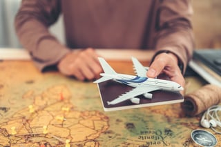 Mani che mostrano un modellino di aeroplano e un passaporto sopra una mappa del mondo e un libro. Lente d'ingrandimento e bussola. Mani che mostrano un modellino di aeroplano e un passaporto sopra una mappa del mondo e un libro. Lente d'ingrandimento e bussola.